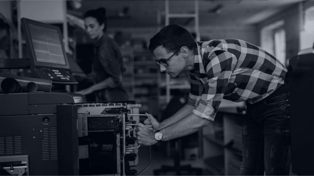 Black and white image of man bending down looking at printer