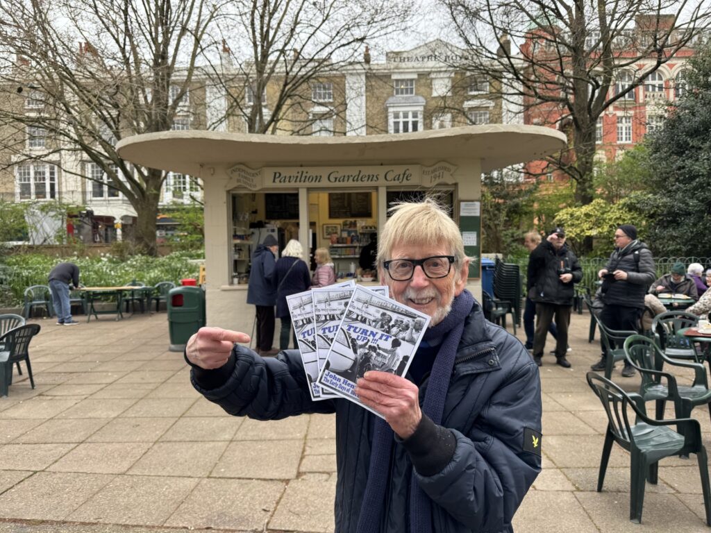 Image of John Henty holding his fourth book in front of Brighton Pavilion Gardens Cafe